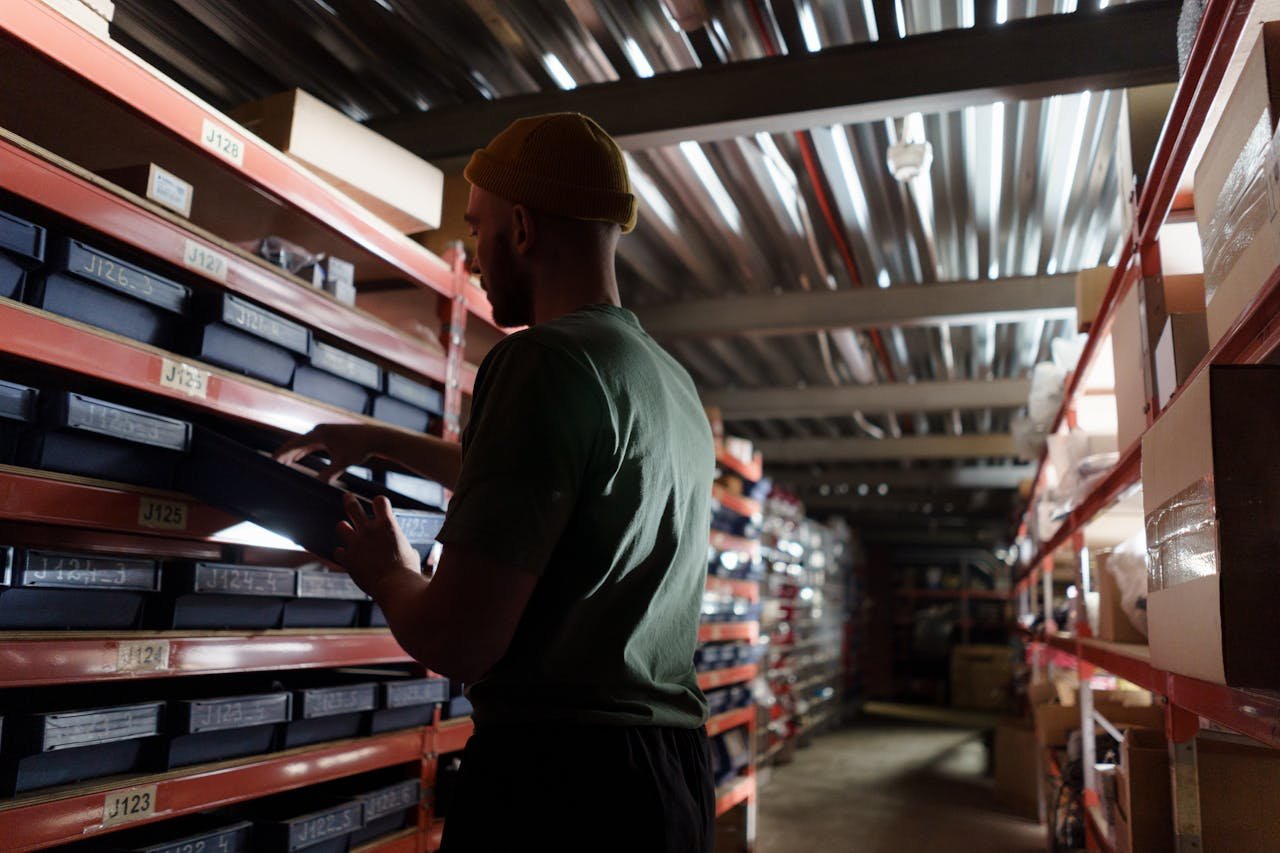 A man organizing inventory on shelves in a dimly lit warehouse, wearing a uniform.