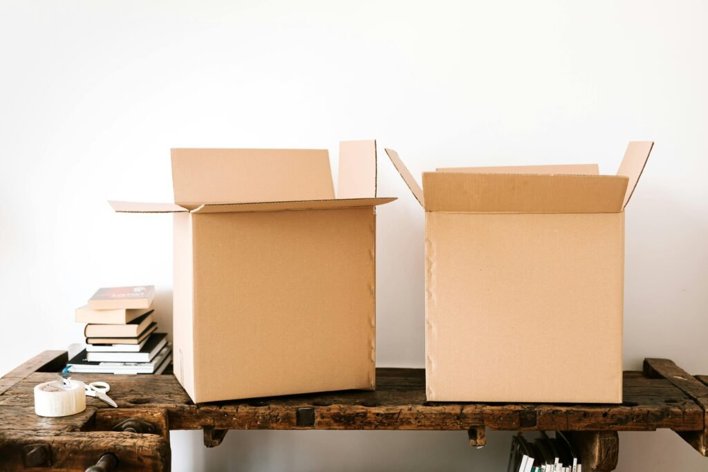 pexels-photo-4498124-4498124 Opened carton boxes and stacked books placed on shabby wooden desk with tape against white wall